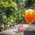 A glass of spiked apple cider on a table in the Garden, surrounded by tropical blooms.