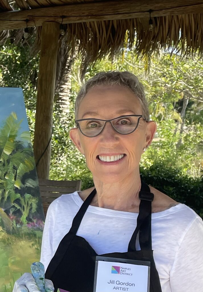 A smiling person with glasses wearing a white shirt and a black apron