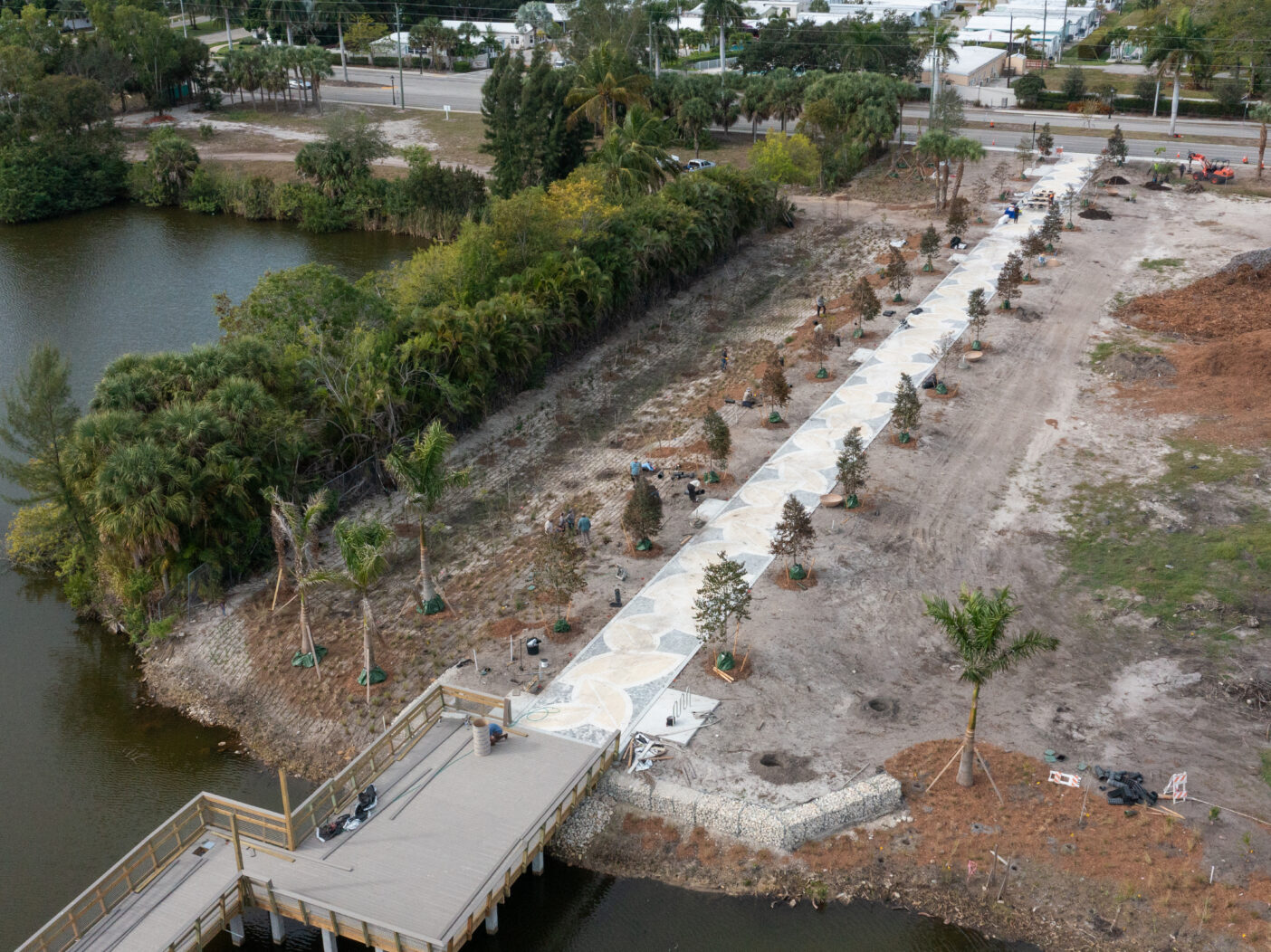 Aerial footage shows a straight, concrete walkway lined with new plantings that meets a section of boardwalk going over water.
