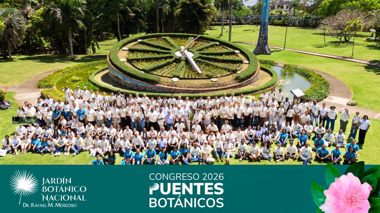 A large group of over 100 people pose for a photo with a garden space behind them. The photo has the logo of the 2026 Botanical Bridges conference across the bottom. 