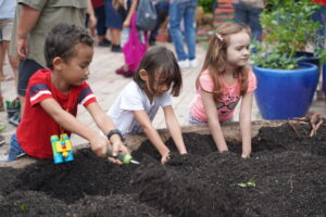 Three children have their hands deep in a garden bed full of dirt.