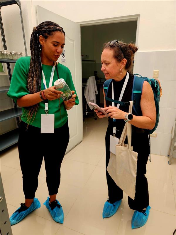 Two people stand in a plant lab and inspect the contents of a small jar.